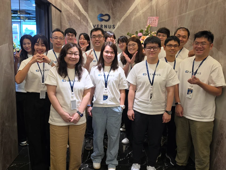 The Vernus AI team in front of the company logo wall